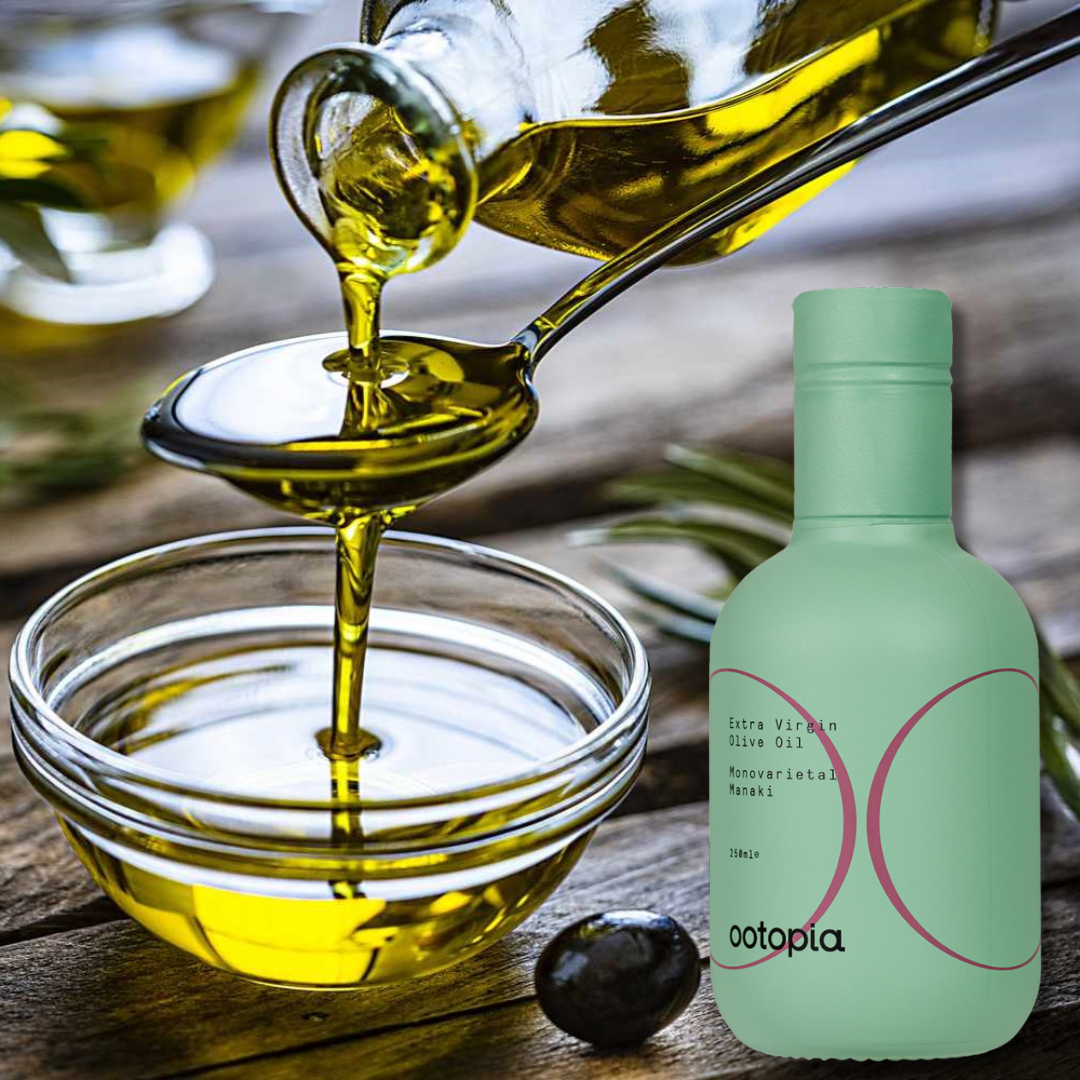 Pouring extra virgin olive oil into a spoon above a glass bowl; Ootopia Manaki bottle on a rustic table.